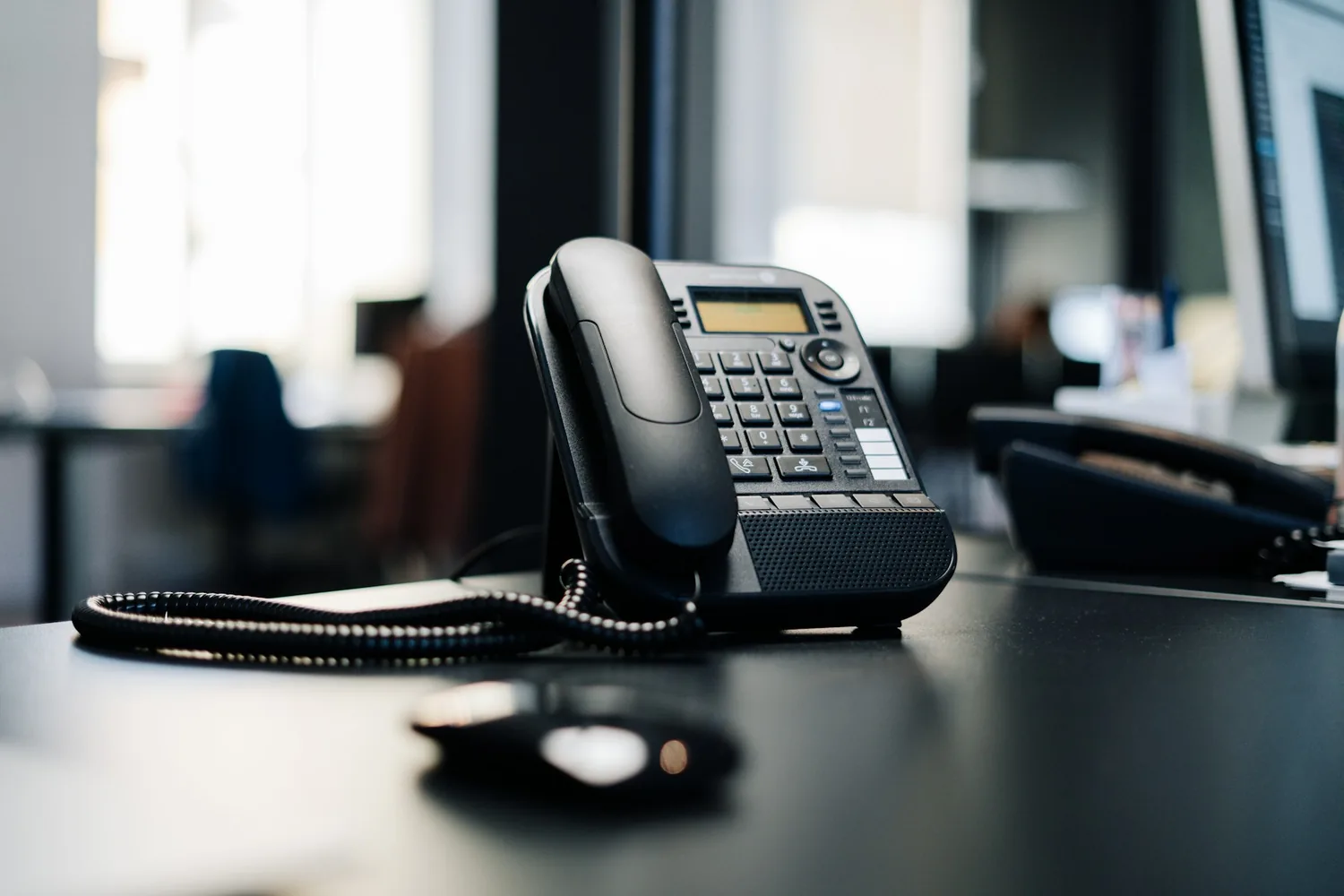 Poste téléphonique de bureau posé au premier plan, le reste de l’agence flou derrière