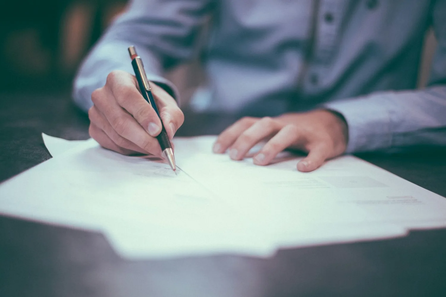 Main tenant un stylo au-dessus d’un document posé sur une table