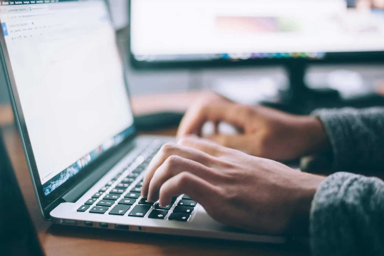 Des mains tapent sur un ordinateur portable ouvert sur un document, un écran d’ordinateur flou à l’arrière-plan
