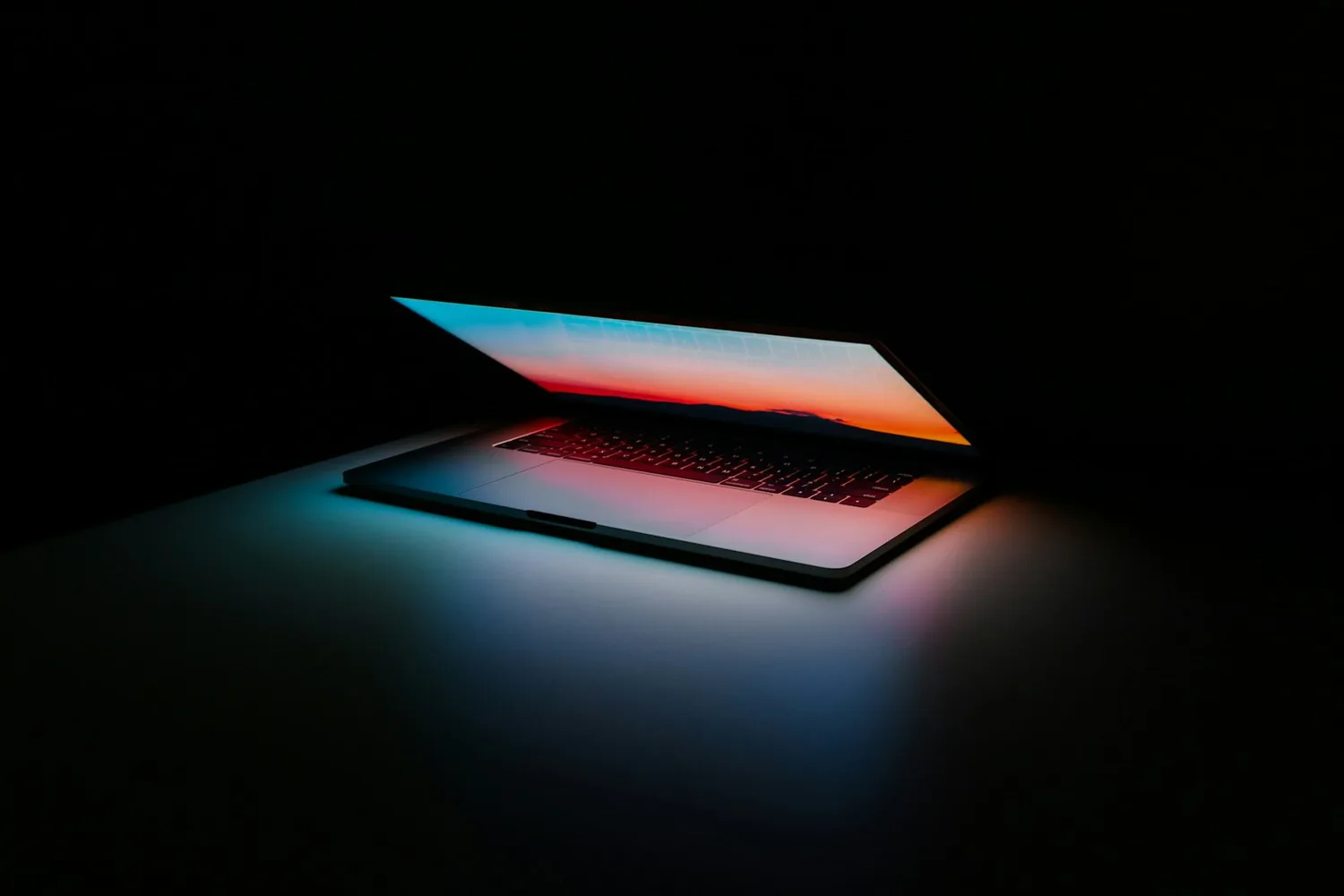 Ordinateur portable entrouvert dans une pièce sombre, son écran coloré éclairant la table