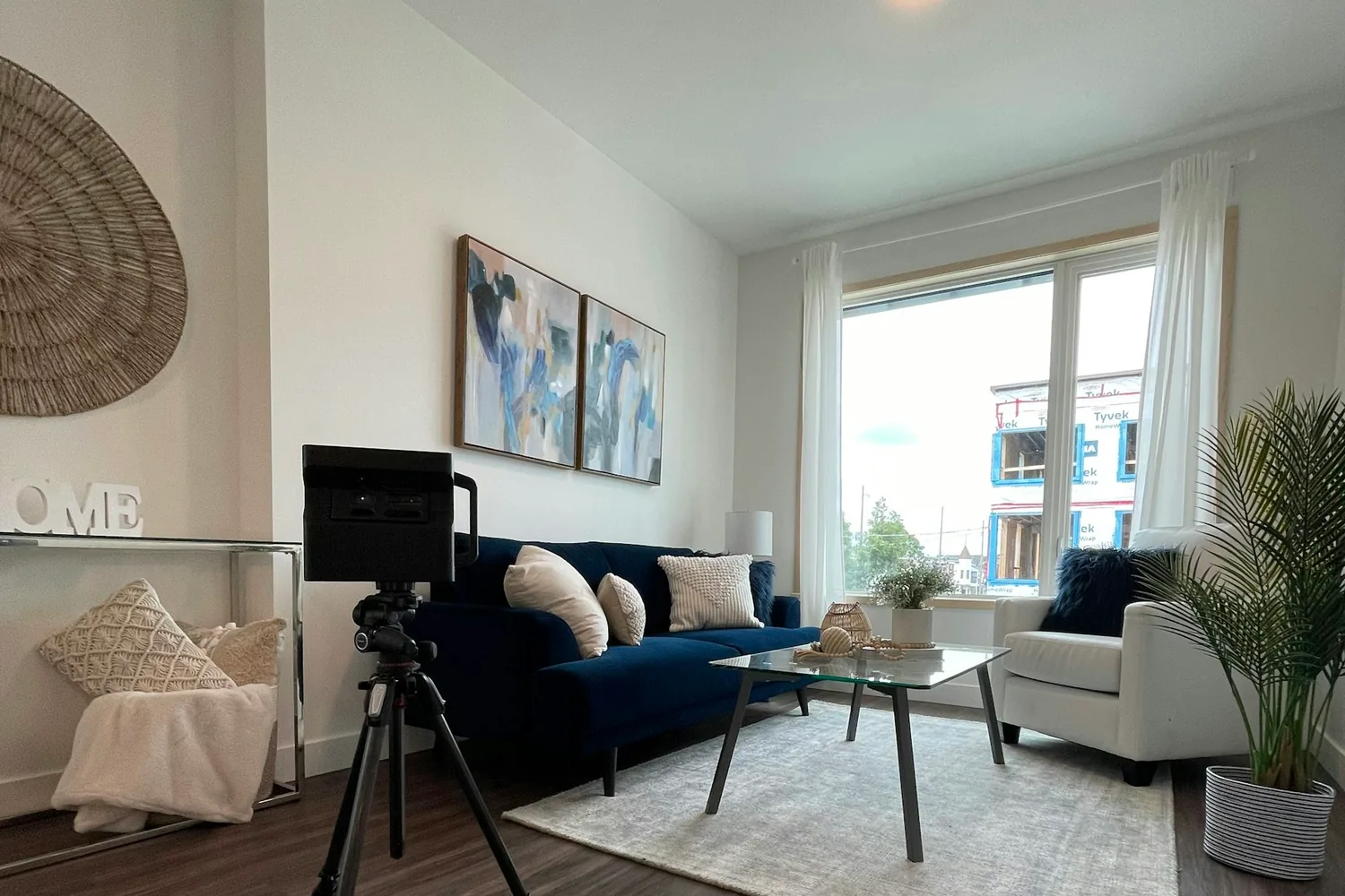 Appareil photo sur trépied installé dans un séjour meublé, face à la baie vitrée