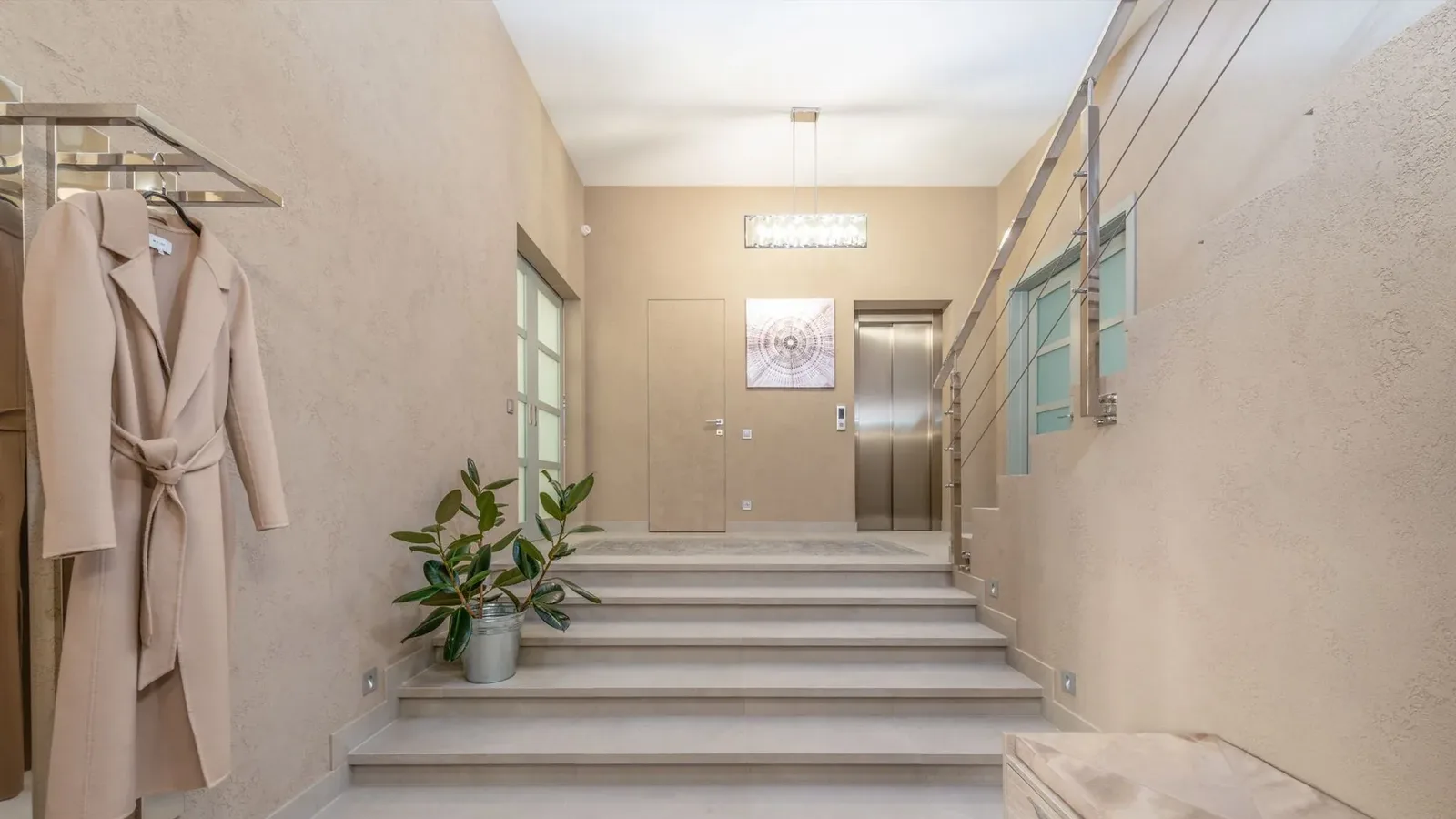Hall d’entrée d’une résidence, escalier en pierre claire, ascenseur au fond, manteau suspendu et plante verte