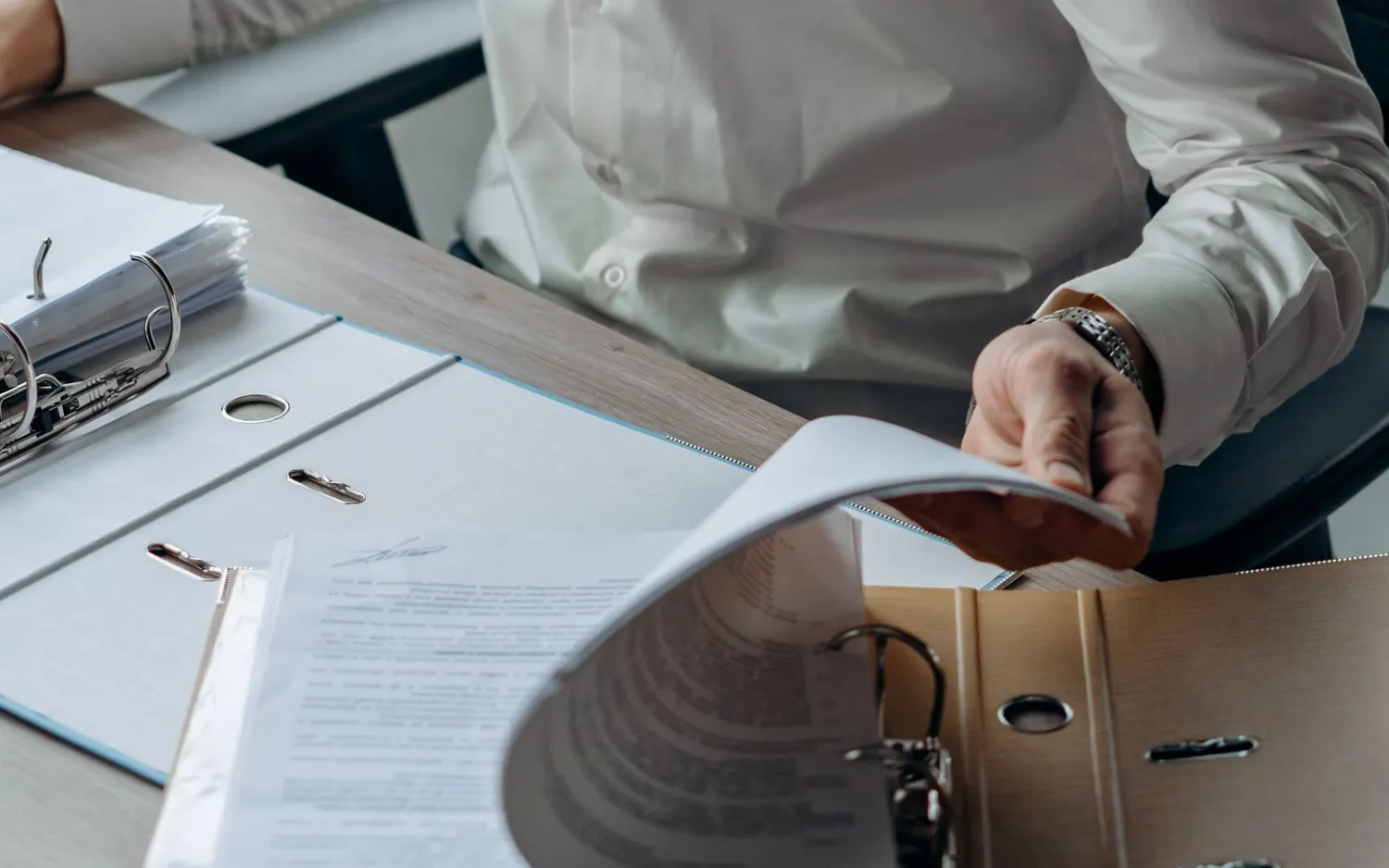 Des classeurs ouverts sur un bureau, une main feuillette un document