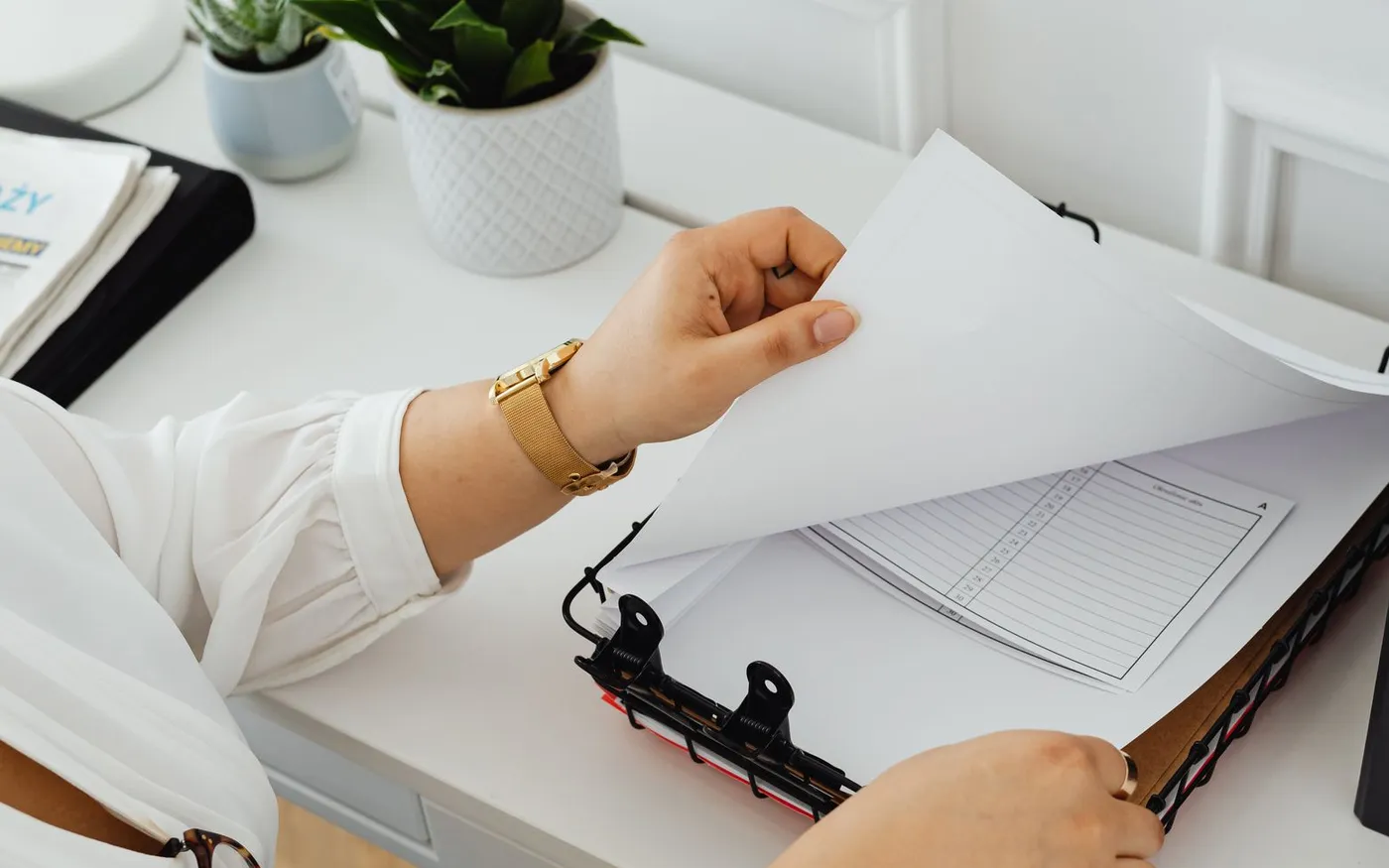 Des mains classent des documents dans un parapheur, sur un bureau clair