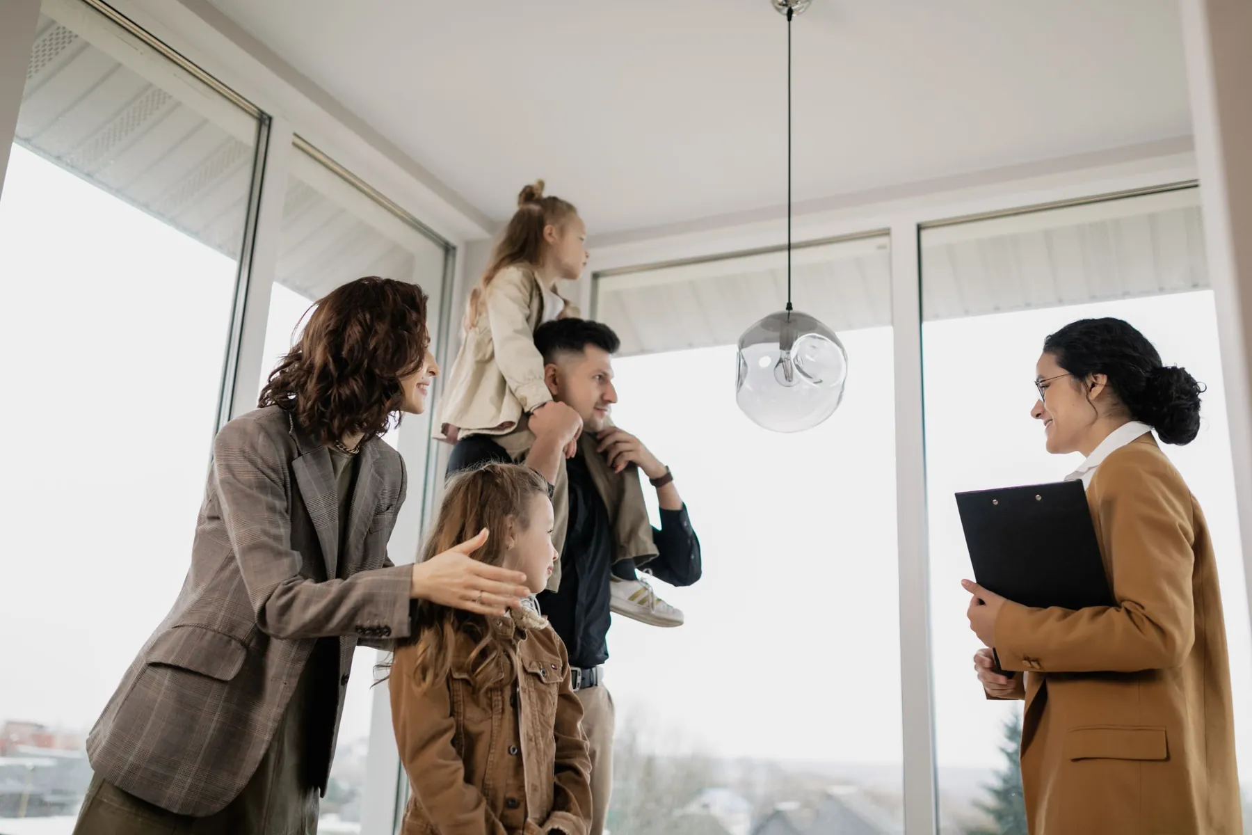 Une conseillère immobilière fait visiter un appartement lumineux à une famille, devant de grandes baies vitrées