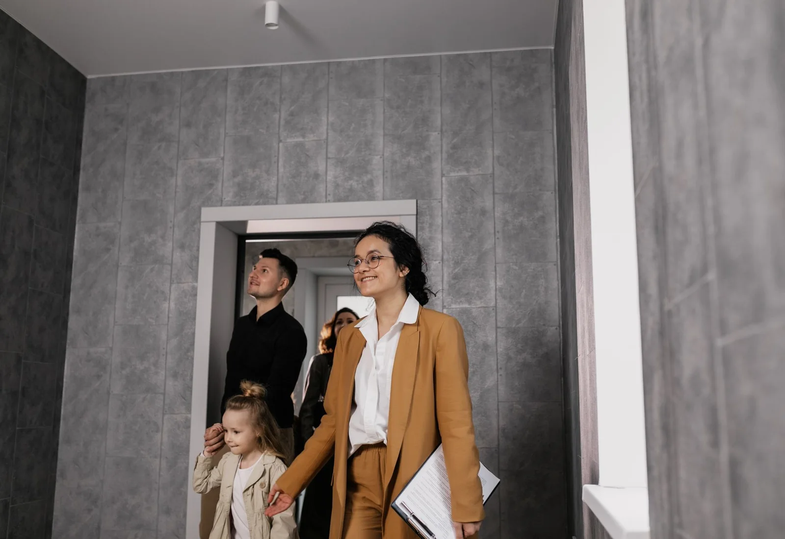Une agente immobilière, un dossier sous le bras, précède une famille dans un appartement