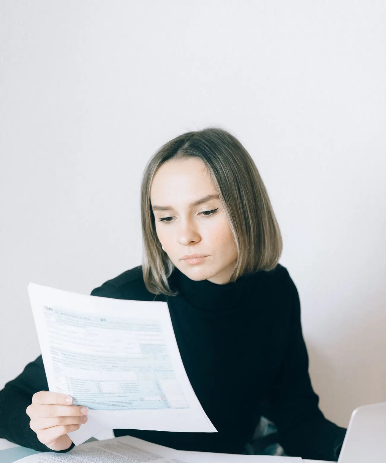 Une jeune femme en pull noir lit attentivement un document imprimé