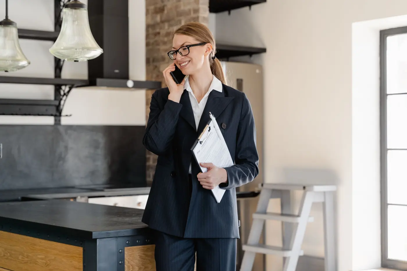 Une mandataire en tailleur téléphone, son bloc-notes à la main, dans un logement