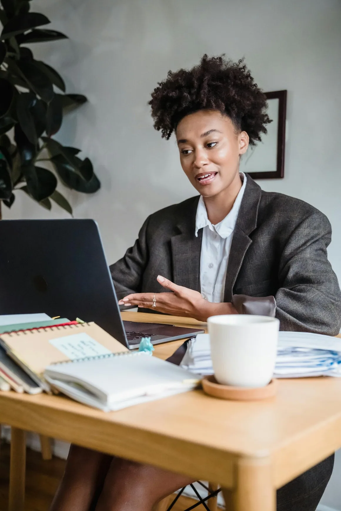 Une professionnelle en veste s’adresse à l’écran de son ordinateur portable, des carnets et une tasse sur la table