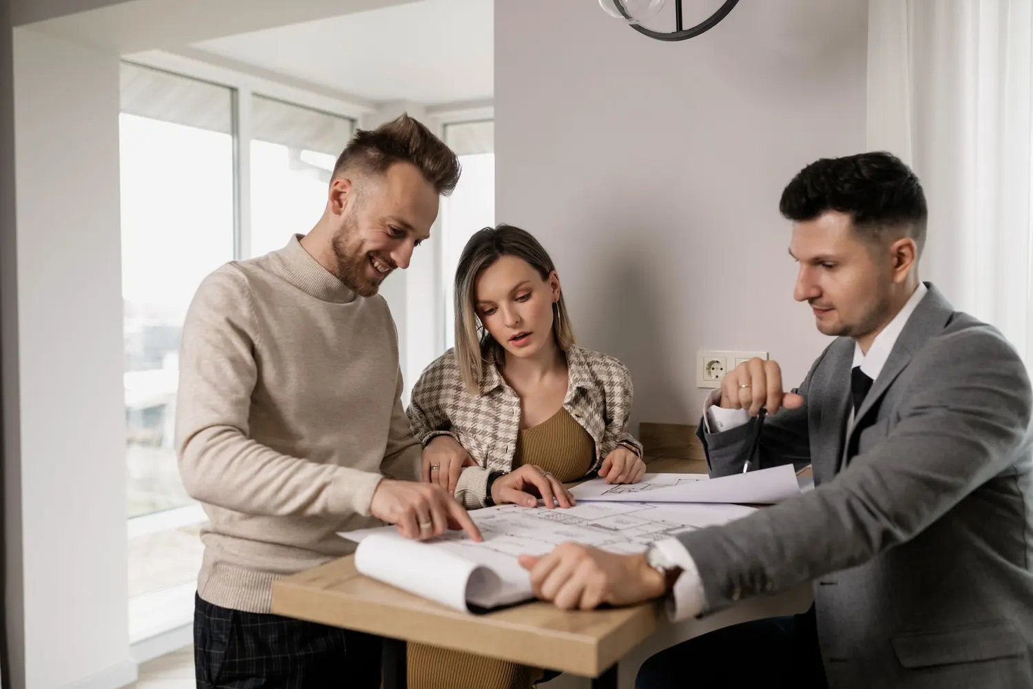 Un agent immobilier et un couple penchés sur des plans, autour d’une table