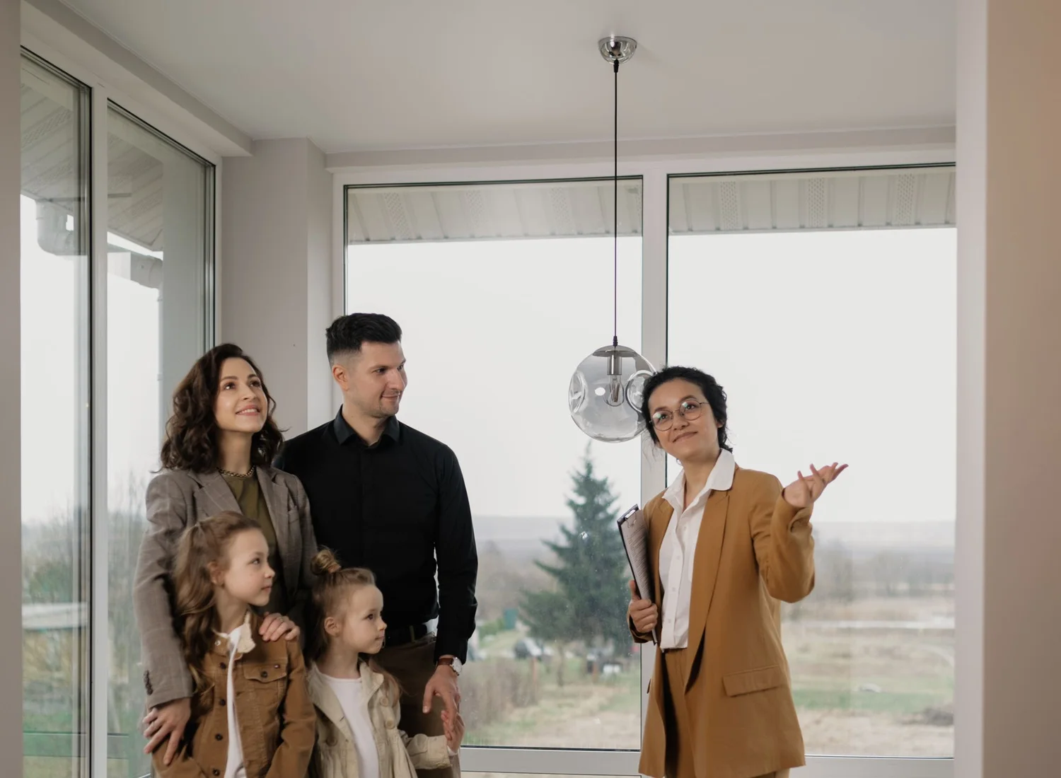 Une conseillère immobilière fait visiter un logement vide à un couple et à leurs deux filles, devant une grande baie vitrée
