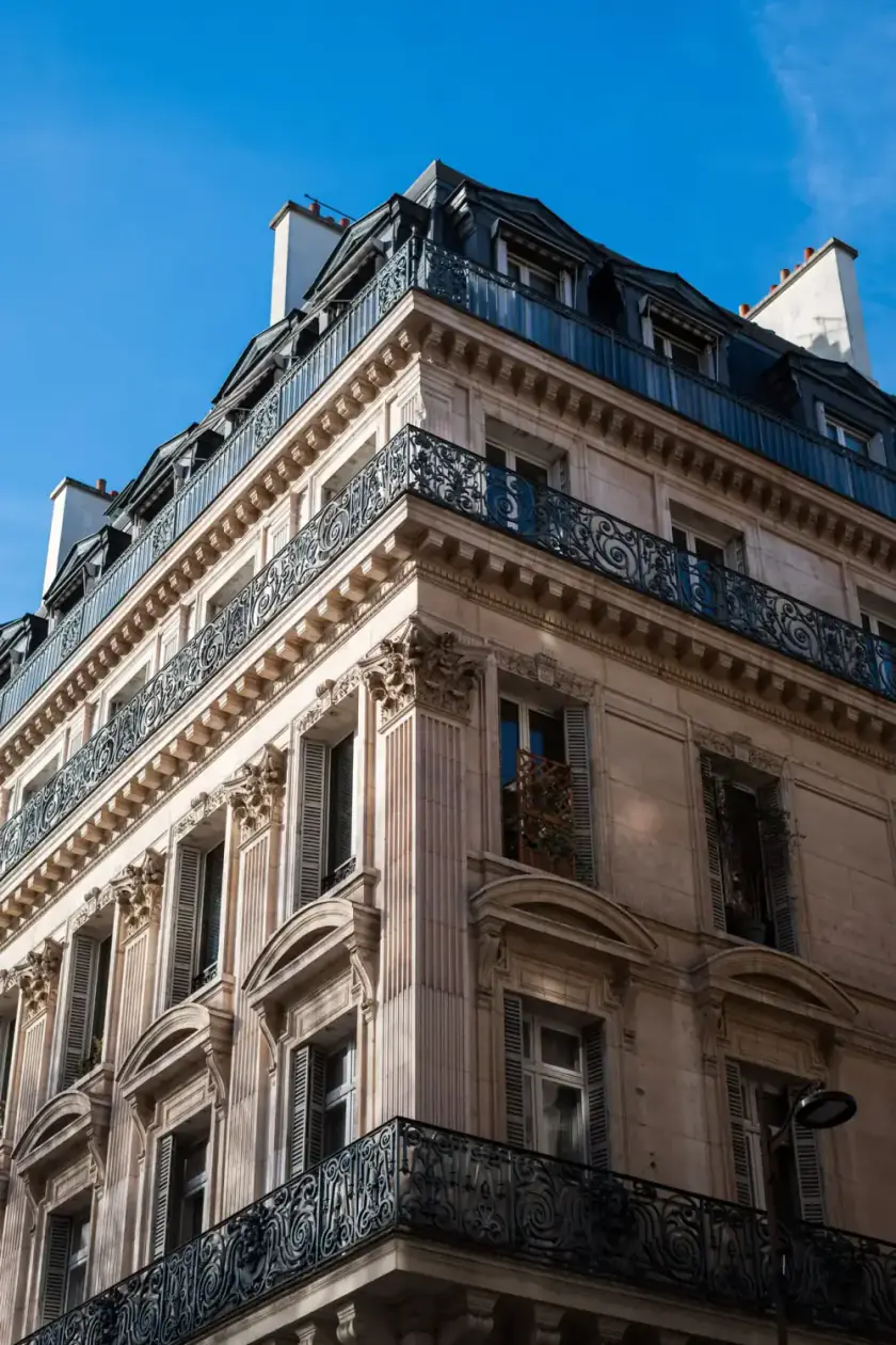 Angle d’un immeuble haussmannien parisien, balcons en fer forgé sous un ciel bleu